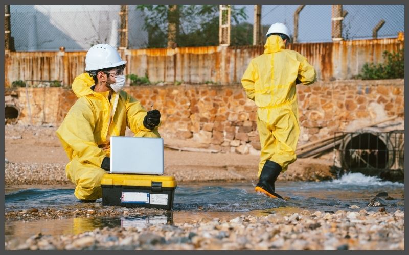 Two men in a construction yard gathering tests, wearing yellow suits