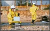 Two men in a construction yard gathering tests, wearing yellow suits